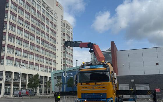 a yellow and blue truck parked with a crane arm extended near a building construction site showcasing equipment for hire and lifting four construction materials