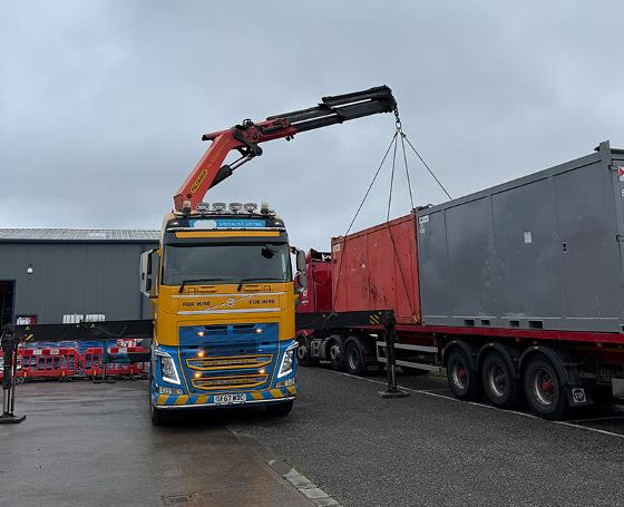 a yellow and blue for hire truck with a crane extending towards a building under a cloudy sky in an urban setting near a university perfect for construction projects with 13 uses of lifting equipment